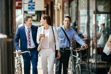 Diverse colleagues walking together with bicycles and coffee in city