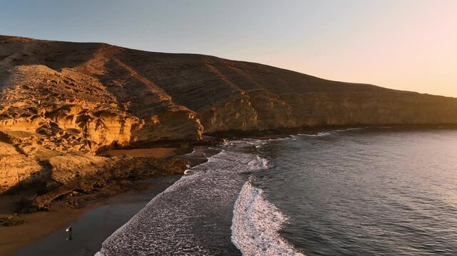 Aerial view of sunrise over the ocean with waves crashing on the beautiful beach and cliffs, Arico, Spain.