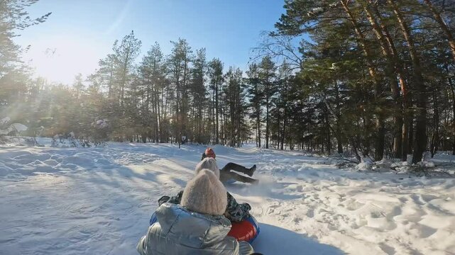 POV shot of snow tubing down hill in winter forest with little friends, children doing fun activity on winter vacations