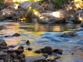 Water flowing in the Virgin River, reflecting the golden color of the surrounding Navajo sandstone cliffs in Zion National Park in Utah