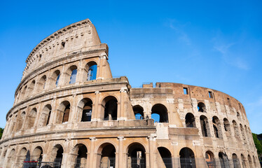 Obraz premium The majestic Colosseum stands proudly under a clear blue sky in Rome, showcasing its ancient architecture and historical significance. Visitors admire its grandeur and rich history.