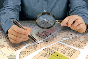 SEARCHING BUILDING PLOT FOR HOME CONSTRUCTION - Hand with magnifier on fictional cadastral map and...