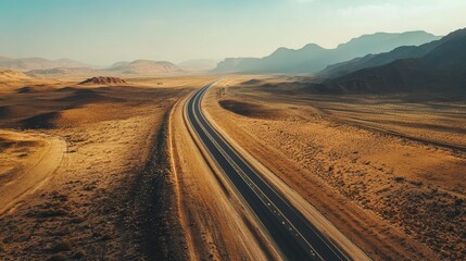 Fototapeta premium Aerial view of a long, winding road through a vast desert landscape under a clear sky.