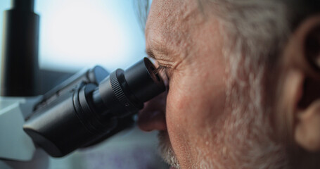 Close up of mature microbiologist conducting fossil analysis under microscope. Scientist or archaeologist working with professional equipment in advanced archaeological science lab. Scientific method.