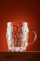 An empty beer glass on a wooden stand on a red background, one object close-up view