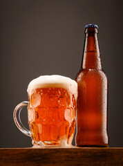 A bottle of beer and a glass of beer on a dark background.