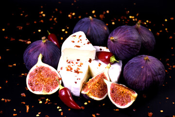 Whole and cut figs with cheese and pepper on a black background. Spicy taste. Mediterranean cuisine.