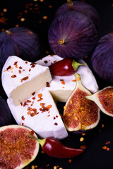 Whole and cut figs with cheese and pepper on a black background. Spicy taste. Mediterranean cuisine.