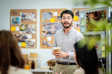 A man is holding a cardboard box and is standing in front of a white board. He is giving a presentation and is holding the box up to show something