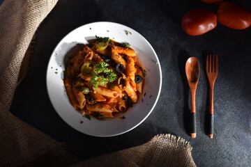 Top view plate of Penne Arrabbiata pasta on dark background. Plate of freshly cooked Penne all'Arrabbiata pasta vertical shot,