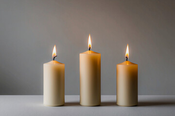 Candles in a Row. Three simple, white candles with golden flames, aligned horizontally on a plain background. The candle flames give off a soft, warm glow, to evoke a cozy, festive atmosphere