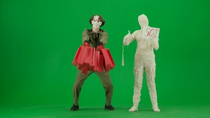 Portrait of person in mummy bandage on chroma key green screen background. Maniac with handful of gift bags, mummy shows sale 50 percent sign thumbs up.