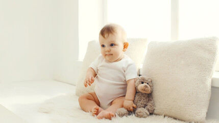 Happy cute little baby playing with teddy bear toy in white room at home