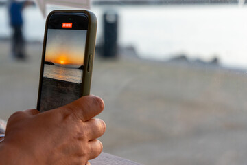 Fototapeta premium A close-up shot of a smartphone capturing a vibrant sunset, with the sun's golden rays reflecting on the screen, blending the colors of the sky with the phone’s sleek design.