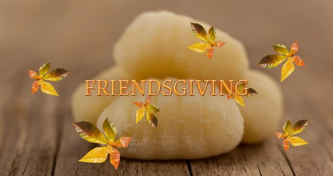 Animation of friendsgiving text over autumn leaves and bread rolls on wooden boards