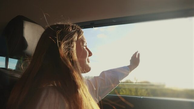 girl driving a car. car ride concept. happy young girl with long hair drives a car with her hand out the window and smiling, with the bright glare of the lifestyle sun. car ride girl