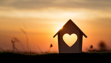 Miniature house with heart shape window on sunset background. Sweet home concept. Family warmth, love and protection