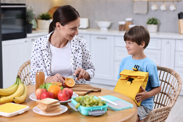 Mother and her cute son preparing lunch box with healthy food at wooden table in kitchen