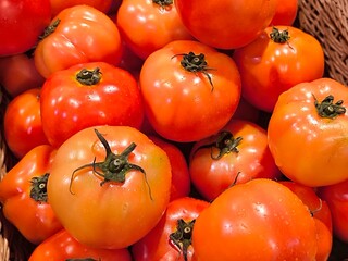 Fresh organic tomatoes in woven basket at supermarket's vegetable zone. Healthy eating. Vegan concept