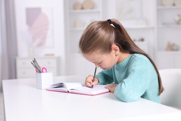 Girl with incorrect posture doing homework at white desk indoors