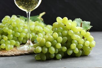 Fresh ripe grapes and glass of wine on grey table, closeup
