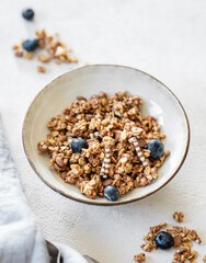 Granola with blueberries in a bowl on a light background with fresh berries, napkin and morning sunlight close up.