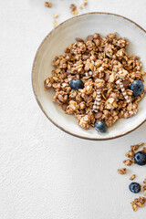 Granola with blueberries in a bowl on a light background with fresh berries and morning sunlight.