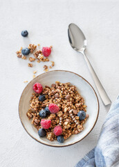 Dry muesli or granola, raspberries and blueberries in a bowl on a light background with fresh berries, spoon and morning sunlight.