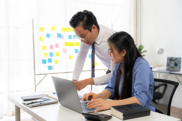 Collaborative Brainstorming: Asian business professionals engage in focused discussion, utilizing a laptop and sticky notes for innovative problem-solving in a modern office setting. 