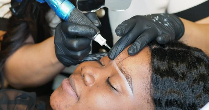 Beauty therapist apply permanent makeup to client eyebrows in salon using rotary pen tattoo machine