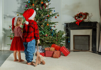 Small children in Santa hats admire a decorated Christmas tree