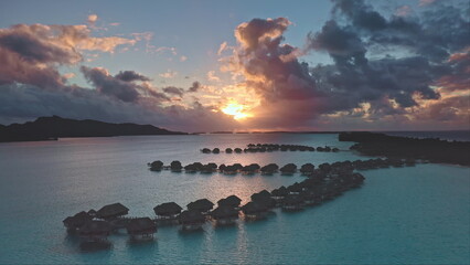 Dramatic colorful sunset sky over Bora Bora with overwater bungalows silhouette, turquoise lagoon...