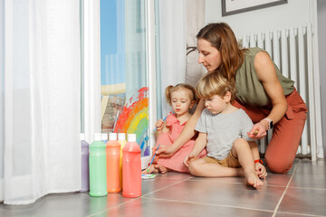 Pair of kids joyfully painting a rainbow on sliding glass door