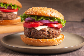 Homemade delicious hamburger with beef, onion, tomato, lettuce and cheese. Fresh burger close up on wooden rustic table with potato fries. Cheeseburger. Burger.