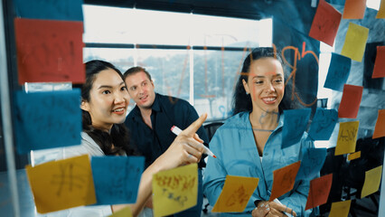 Portrait of professional diverse business team brainstorming marketing idea on colorful sticky notes stuck on glass board. Hispanic project manager write business strategy on note. Manipulator.