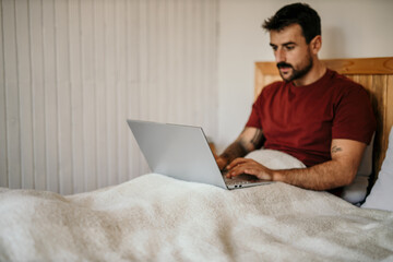 Focused man working on a laptop from the bed