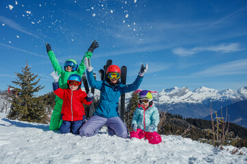 Playful family relax toss snow in the air on sunny snowy slope