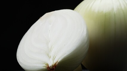A close-up of a fresh peeled onion, sliced paper-thin, placed with black background. White and yellow layers cascade down, each a promise of crisp texture and pungent bite. Macrography. Comestible.