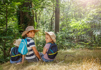 A group of three kids with hats and bags sits on green hillside