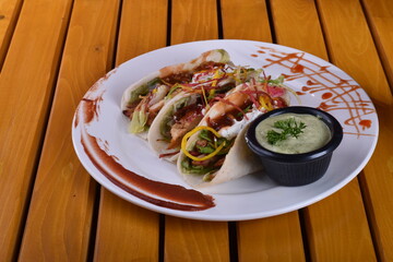 long platter of tacos with a bowl of salsa. Tacos Dorados: Rolled, fried tacos typically filled with shredded chicken or potatoes, served with salsa and crema.