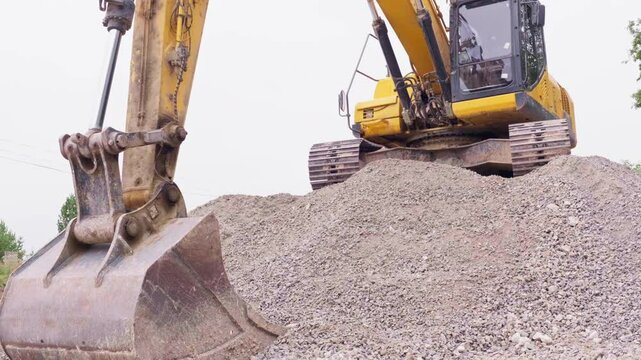 A yellow backhoe loader on a heap of gravel against the sky