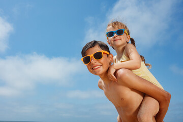 Fototapeta premium Teenager hold his sister on back as they wear bright sunglasses