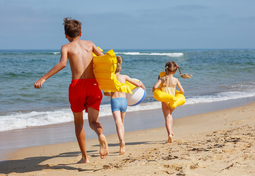 Three kids enjoy a day at beach with inflatables and beachball