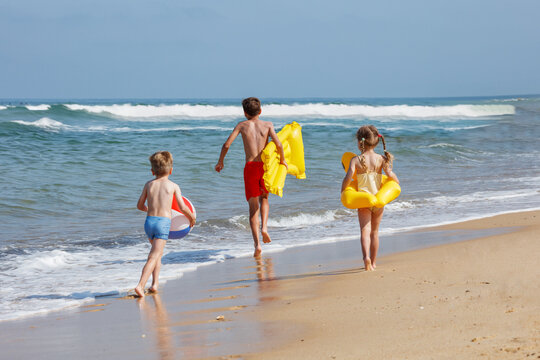 Happy kids play with inflatables and beachball on a sunny beach