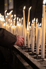 Arm and hand of a person placing a burning candle at an altar in a church.