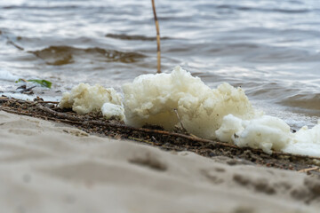 River bank with waves and white foam. White soft foam swaying. Blue water edge on sandy beach. Swirl natural pattern in shallow water. Tranquil scene of beach.