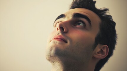 Fototapeta premium A close-up of a man looking up with a slight smile, his face illuminated softly, emphasizing his features against a plain backdrop