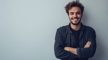 Naklejka premium A charming man with striking features and a warm smile poses casually with crossed arms, set against a plain light backdrop