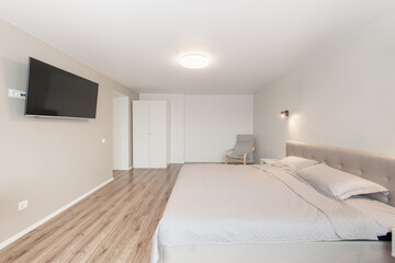 Luxurious master home bedroom interior, modern house, beautiful interiors, wide bedroom. TV Set on the Wall. King Size Bed, White Walls and Ceiling. Hardwood Floor