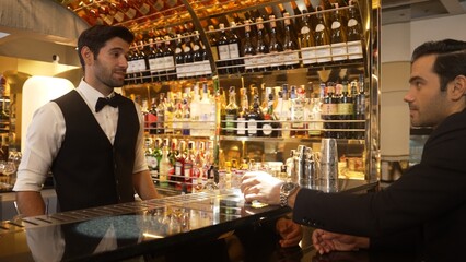 Smart bartender serving drink gin fizz with lemon sliced to VIP guest while waiting friend at luxurious counter bar. Barman providing excellent service at vibrant nightlife party atmosphere. Vinosity.